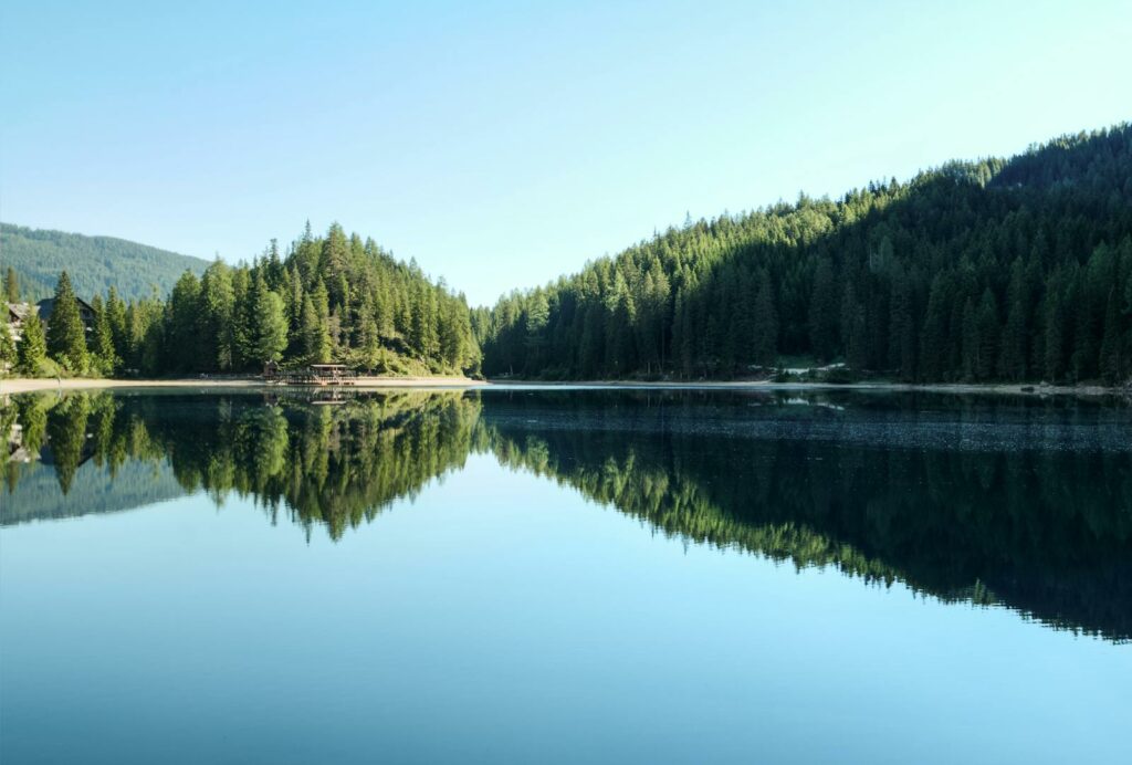 Serene view of a mountain lake with forest reflections and clear blue sky.