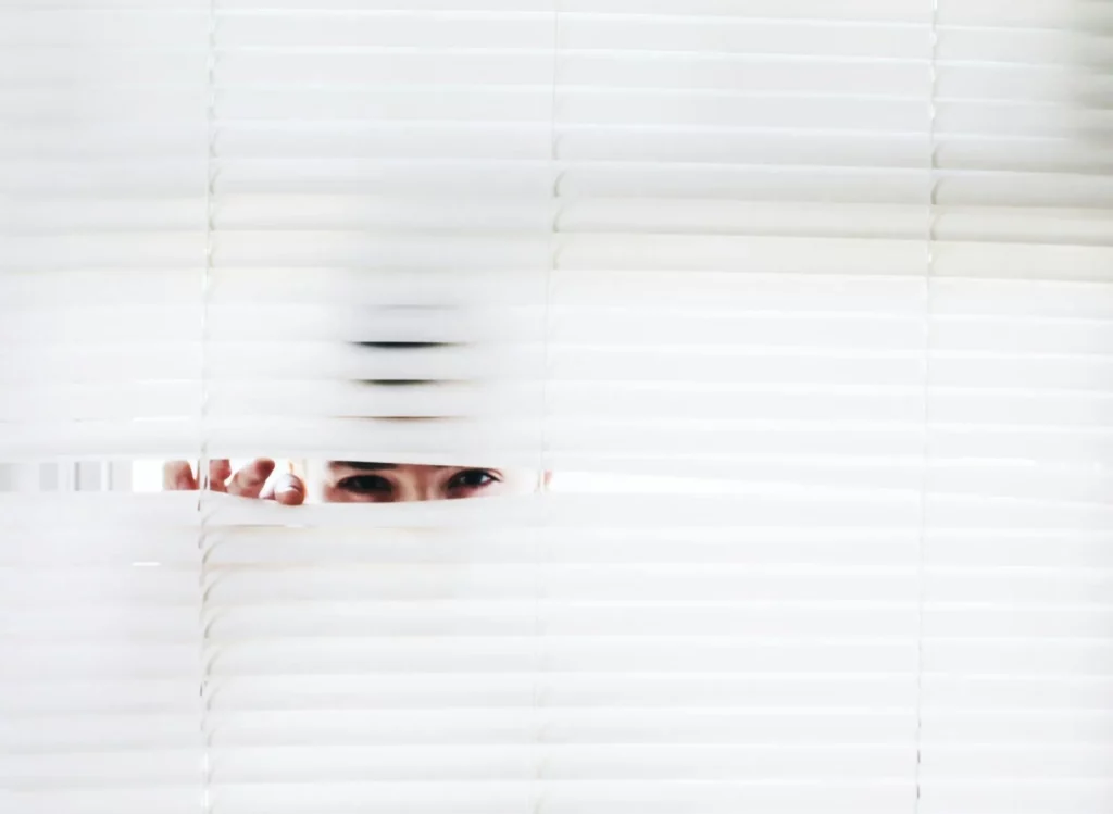 A person peeks through white blinds, creating an intriguing sense of curiosity.