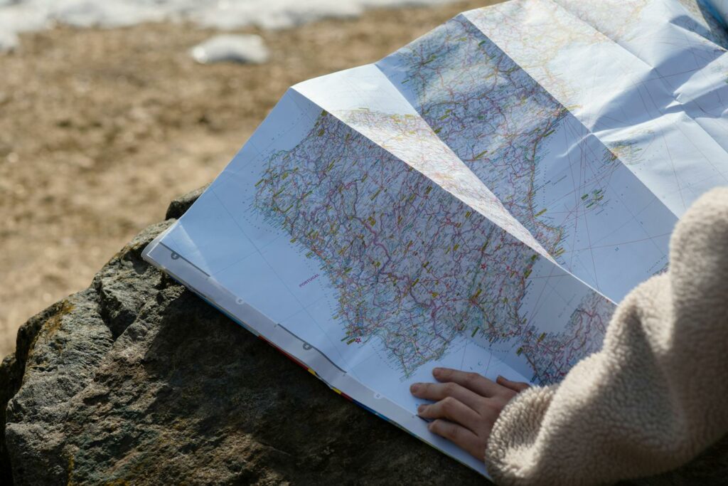 A person studies a roadmap placed on a rock, embraced by natural sunlight outdoors.