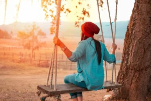 Woman in a beanie on a swing, relishing the sunset in a serene outdoor setting.