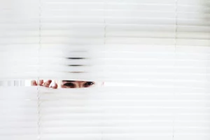 A person peeks through white blinds, creating an intriguing sense of curiosity.